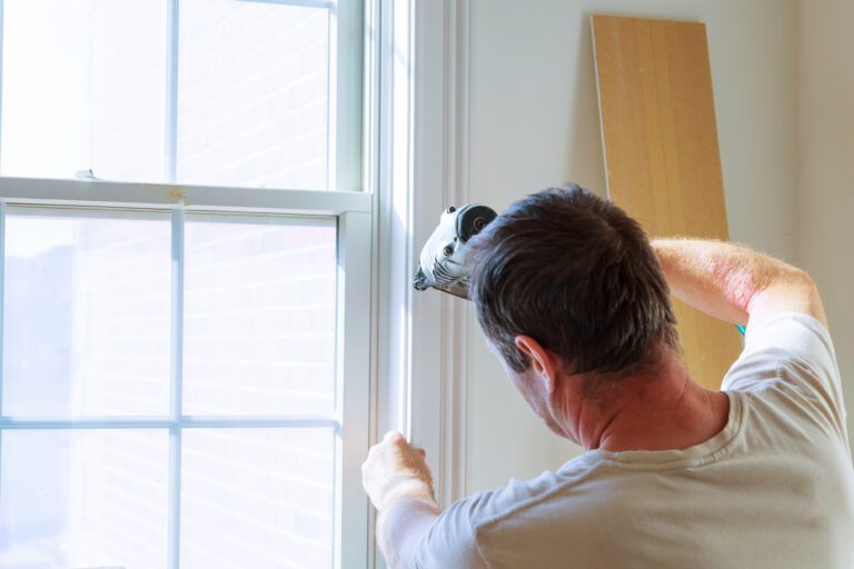 Carpenter using nail gun to moldings on windows, framing trim, with the warning that all power tools have on them shown illustrating safety concept