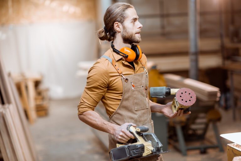 Portrait of a handsome carpenter in uniform with modern tools at the joinery workshop