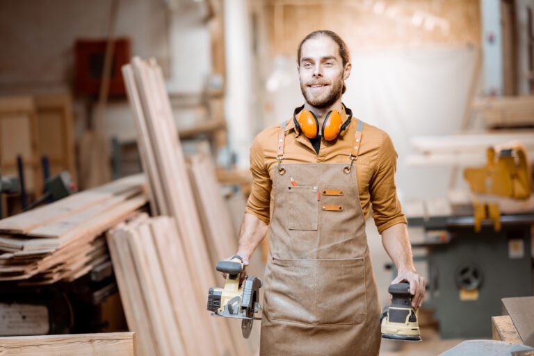 Portrait of a handsome carpenter in uniform with modern tools at the joinery workshop